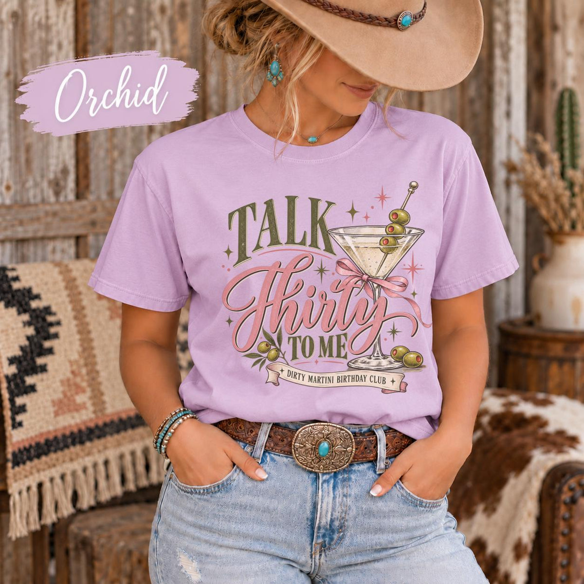 Orchid T-shirt showcasing the dirty martini birthday graphic with olive green and pink lettering, cocktail illustrations, and feminine bow accents.