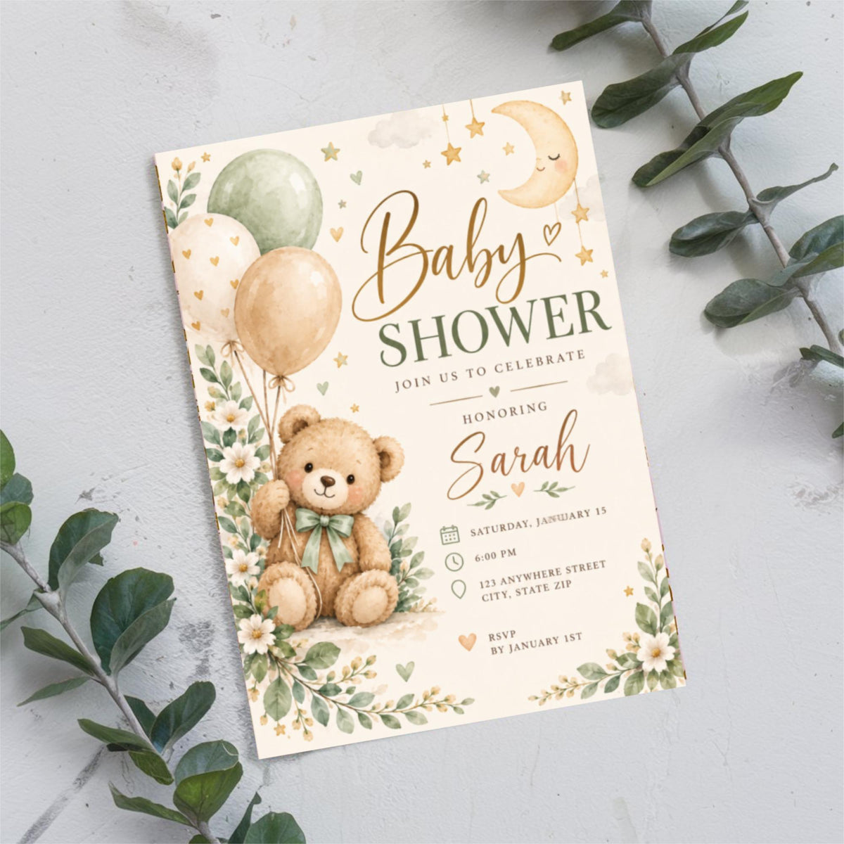 Printable baby shower invitation resting on a light neutral surface surrounded by eucalyptus branches. The whimsical nursery-inspired artwork features a teddy bear, soft pastel balloons, and delicate botanical accents.
