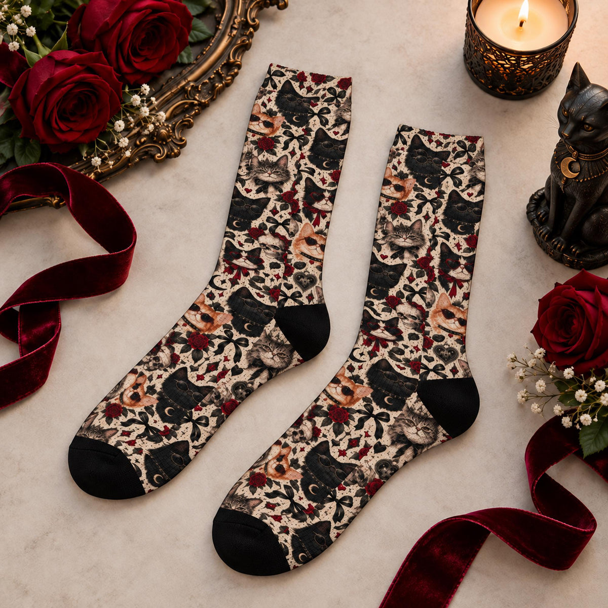 Pair of gothic cat crew socks displayed flat with deep red roses, burgundy velvet ribbon, a candle, and a black cat figurine. All-over vintage cat print features black, gray, and orange cats with floral accents.