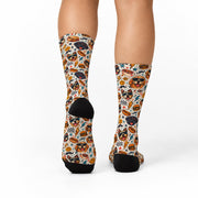 Back view of retro dog crew socks showing the all-over print with smiling dogs, sunglasses, burgers, hot dogs, lightning bolts, and colorful vintage-inspired details on a cream background.