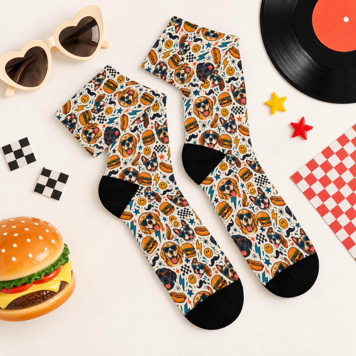 Pair of playful retro dog socks displayed flat with vintage diner accessories, heart-shaped sunglasses, checkerboard decorations, and burger props. All-over design features colorful dog faces, fast food icons, and black toes.
