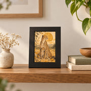Small framed version of the cheetah mother and cub artwork displayed on a shelf beside stacked books and plants.