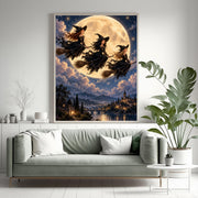 Framed celestial witch wall art displayed above a sage green sofa surrounded by leafy houseplants. The artwork features three witches riding broomsticks beneath a starry night sky and enormous golden moon.