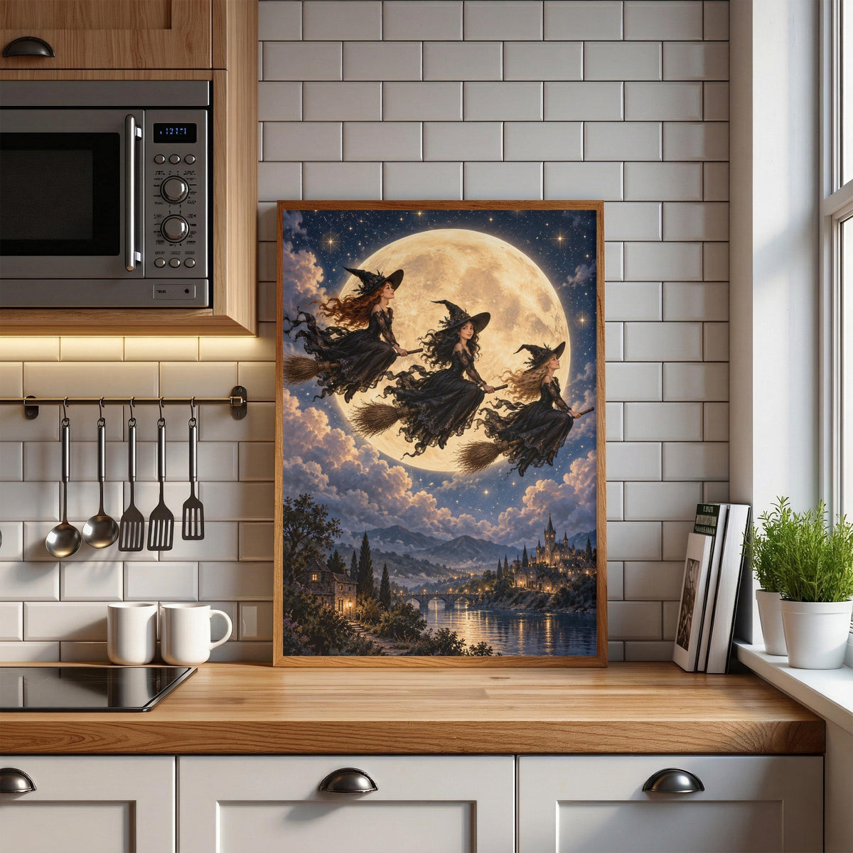 Gothic fantasy printable displayed on a kitchen wall above a light countertop with open shelves and wooden cabinets. The magical poster features three witches flying beneath the stars over a moonlit village.