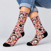 Pair of retro cat crew socks displayed on crossed legs against a neutral studio background. Whimsical print features stylish cats, pink bows, hearts, leopard accents, and contrasting black toes and heels.