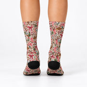 Rear view of women's cowgirl crew socks displaying the all-over vintage western pattern and black heels. Cream-colored socks feature pink boots, floral illustrations, horseshoes, bows, and green cactus accents.