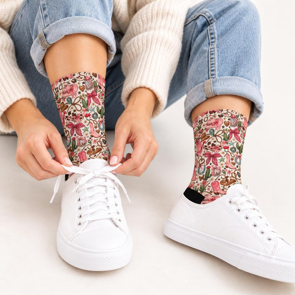Woman wearing pink cowgirl patterned socks with cuffed blue jeans and white sneakers while sitting on a soft pink rug. Playful retro western print features cowboy boots, ribbons, floral details, and green cacti.