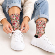 Woman wearing pink cowgirl patterned socks with cuffed blue jeans and white sneakers while sitting on a soft pink rug. Playful retro western print features cowboy boots, ribbons, floral details, and green cacti.