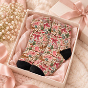 Pair of retro cowgirl socks nestled inside a blush pink gift box with tissue paper and satin ribbon. Girly western design features pink boots, cacti, hearts, horseshoes, and bows, making a cute gift for western fashion lovers.