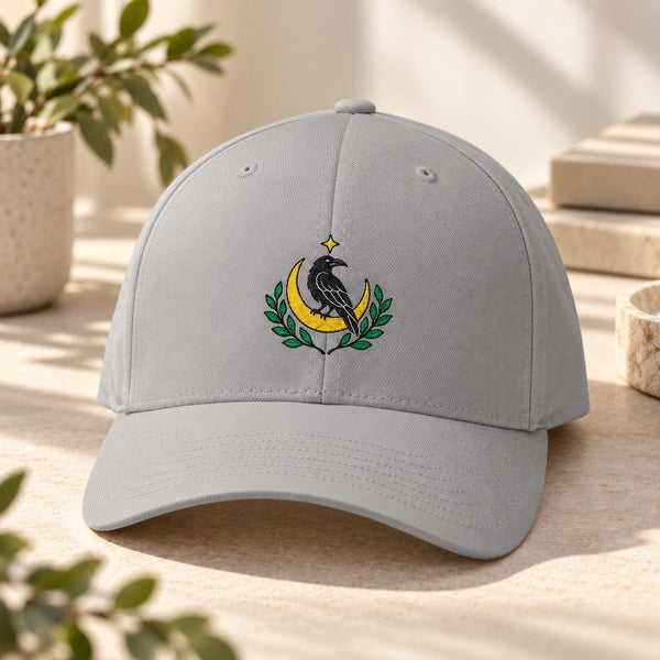 Grey structured Flexfit cap featuring an embroidered black raven perched on a golden crescent moon with green leafy branches and a small star.