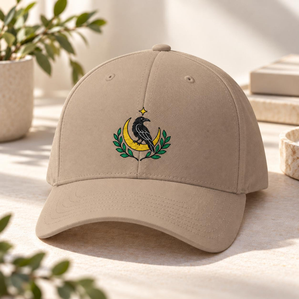 Khaki Flexfit hat showcasing the black bird embroidery with golden moon, leafy branches, and small star detail.