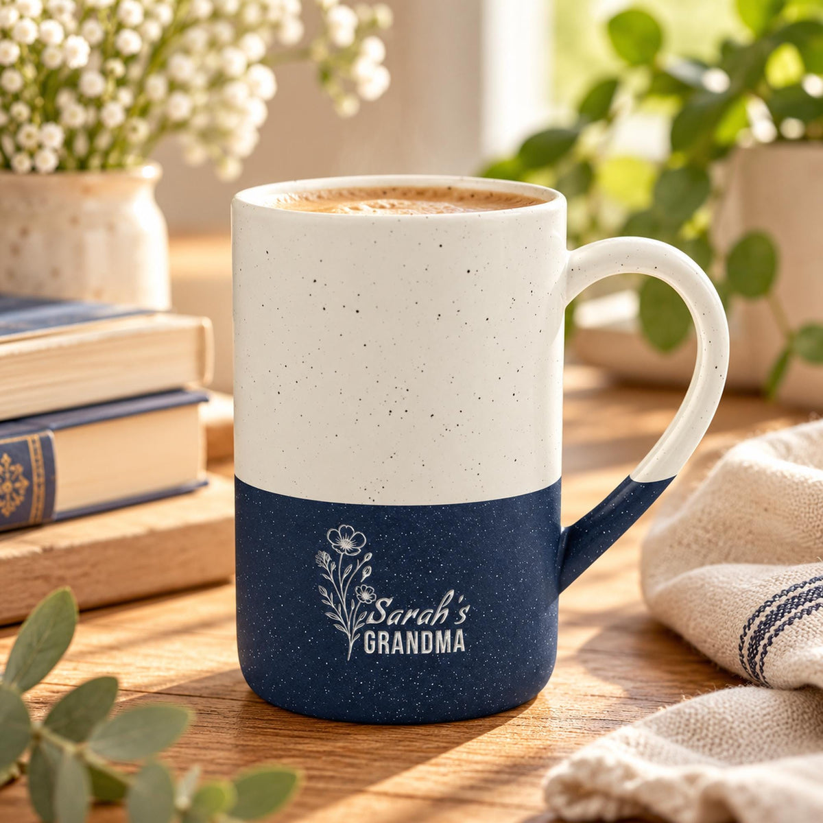 Lifestyle mockup of the 13oz navy two-tone engraved mug filled with coffee and displayed with flowers, cookies, and soft neutral accessories.