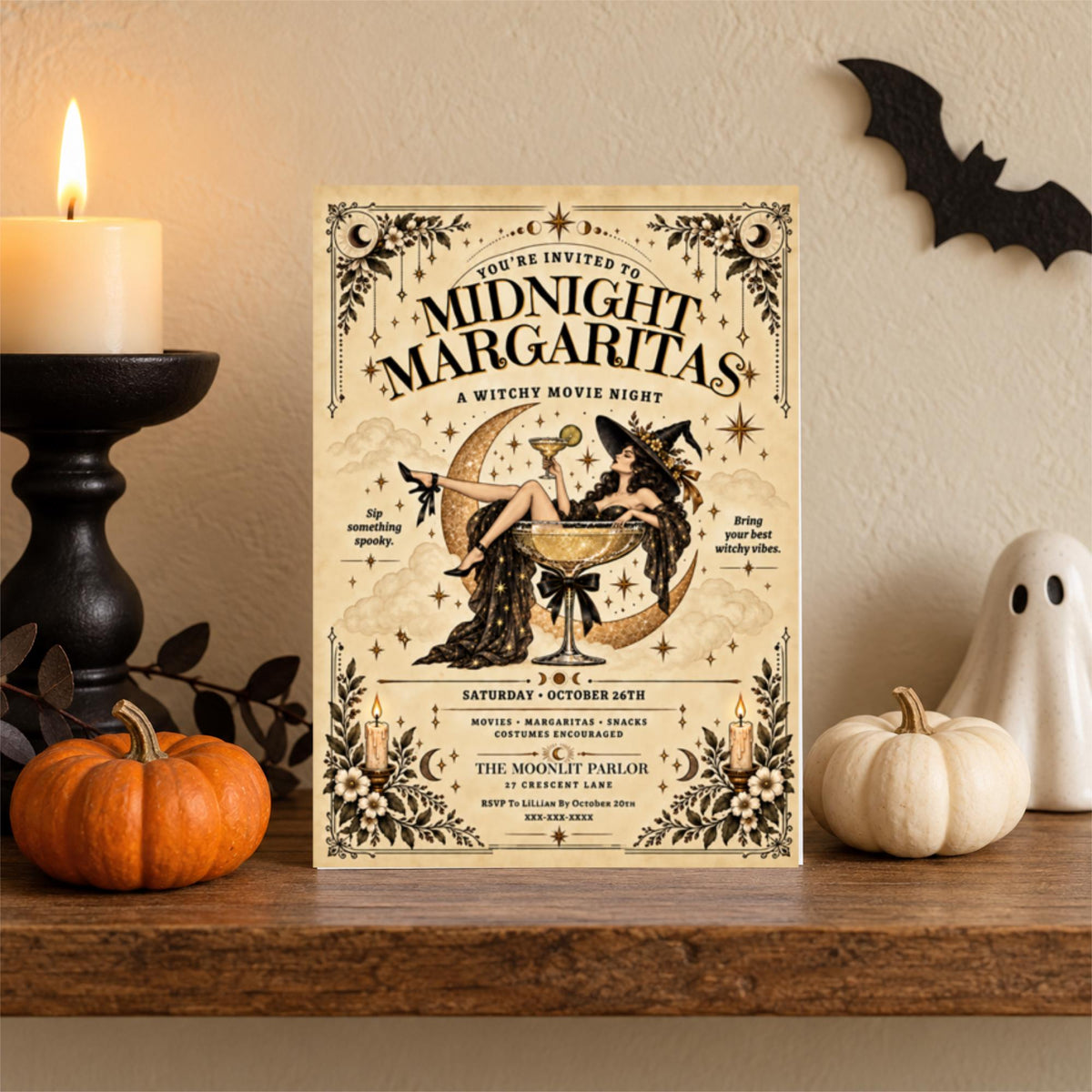 Vintage witch party invitation standing on a wooden shelf beside a black candlestick, orange pumpkin, and small white ghost. The Midnight Margaritas design features antique typography and magical celestial illustrations.