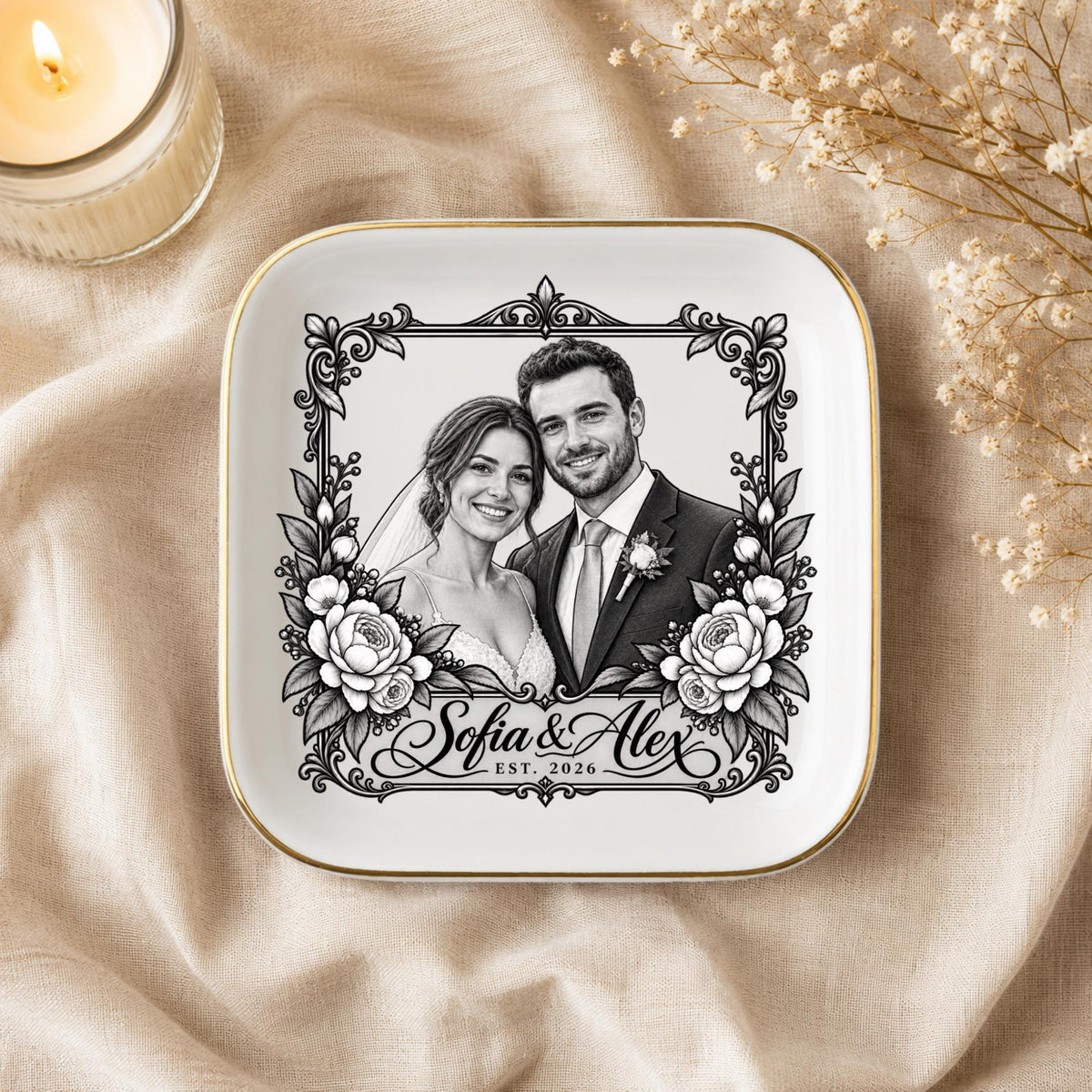 Custom wedding ring dish styled on champagne satin with soft floral accents, gold trim, personalized names, and couple portrait artwork.