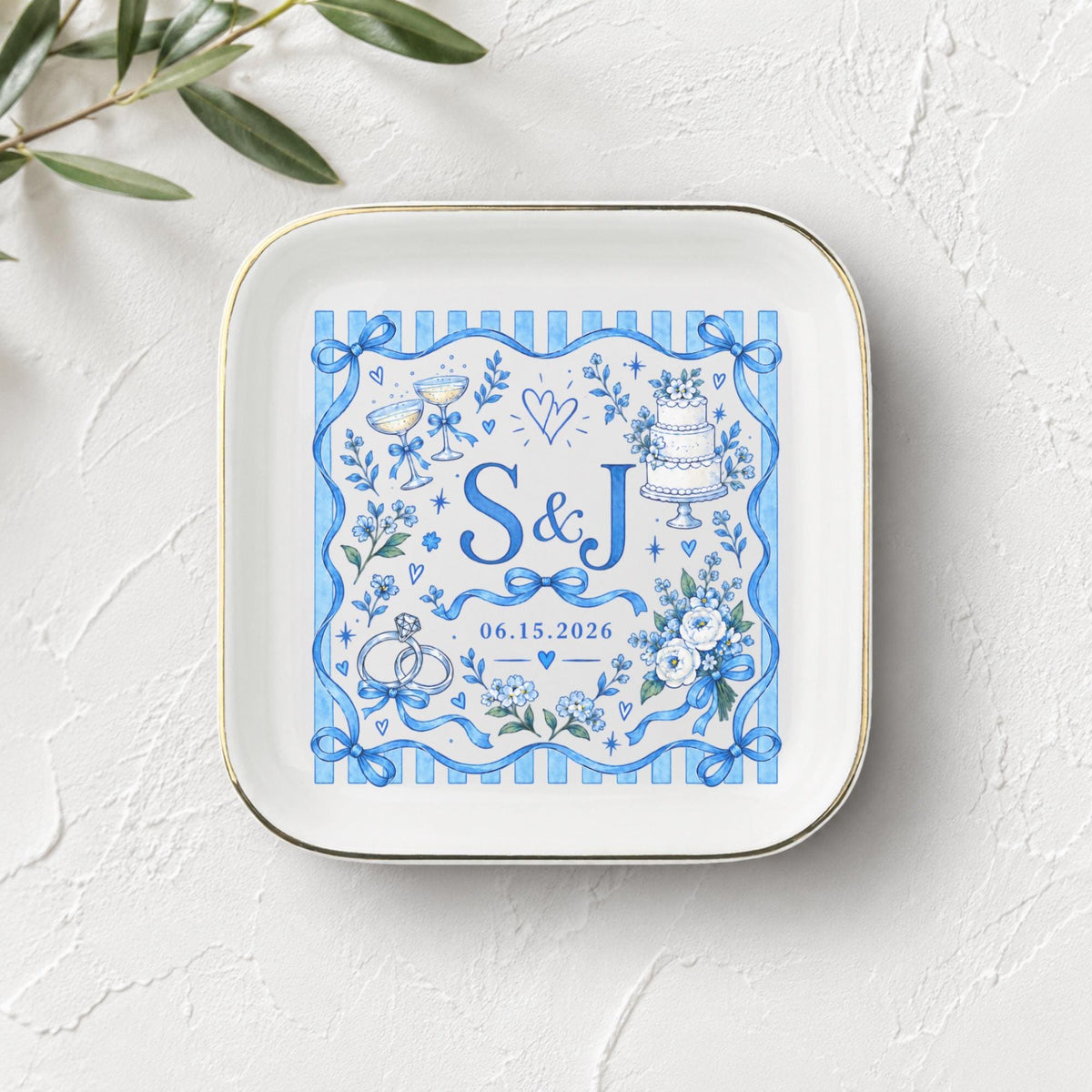 Personalized ceramic keepsake dish shown on a light textured surface with greenery, featuring blue florals, bows, custom initials, and date details.