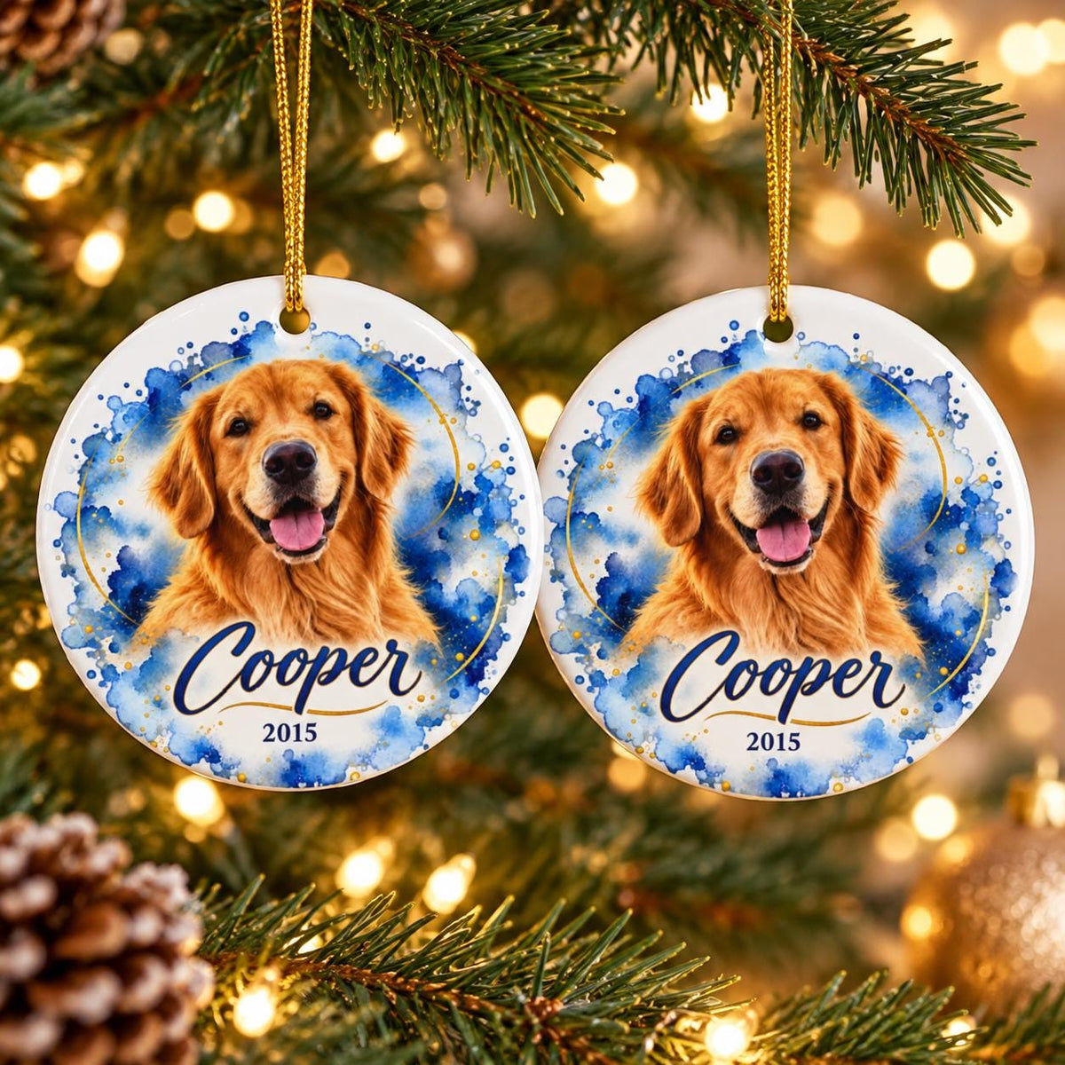 Two matching round ceramic dog ornaments hanging on a Christmas tree, featuring a golden retriever portrait, blue watercolor artwork, gold detailing, and personalized name Cooper with the year 2015.