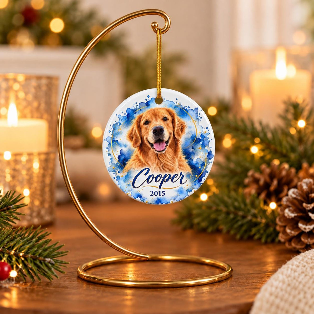 Custom golden retriever photo ornament featuring Cooper's name and year 2015, with blue watercolor artwork and gold details, hanging from a decorative gold tabletop stand beside candles and Christmas greenery.