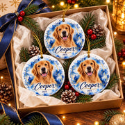 Three personalized ceramic dog ornaments featuring Cooper's golden retriever portrait, blue watercolor design, and gold accents, arranged in a Christmas gift box with tissue paper, pine greenery, and a navy ribbon.