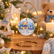 Blue Baby’s First Christmas ceramic ornament featuring a teddy bear, rocking horse, custom name, and date, styled with Christmas greenery and cozy holiday decor.