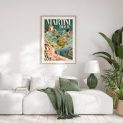 Framed Martini Hour artwork displayed above a white sofa with soft green accents and leafy plants. The retro-inspired poster features a giant cocktail glass, olive garnish, turquoise water, and fashionable women.