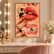 Retro fashion wall art displayed above a makeup vanity with an illuminated mirror, perfume bottles, and soft pink furnishings. The Gloss and Gossip design features oversized glossy lips, red manicured nails, and a woman in a chic black cocktail dress.
