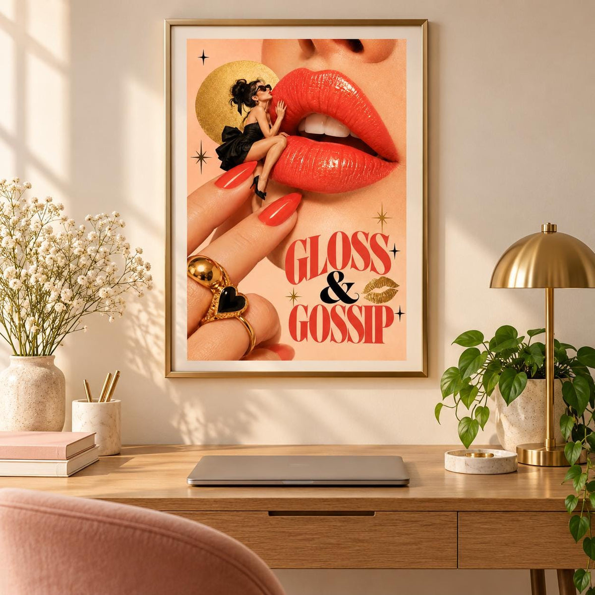 Framed surreal pop art poster displayed above a wooden desk with a gold lamp, small houseplant, and neutral accessories. The Gloss and Gossip illustration adds a playful feminine touch with oversized red lips, glamorous fashion details, and retro lettering.