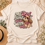 Styled cream T-shirt displaying My Dog Thinks You're Weird Too printable artwork with pink hearts, fluffy dog illustration, and retro typography.