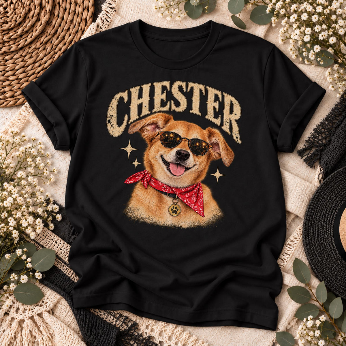 Black T-shirt flat lay showing the personalized Chester dog illustration with cream vintage lettering, sunglasses, red bandana and distressed graphic details in a coordinated boho setting.