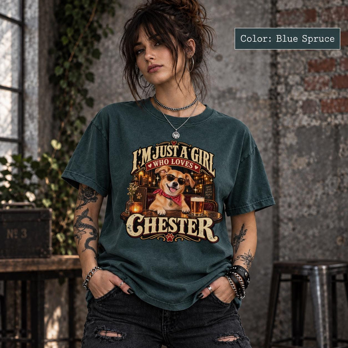 Woman wearing a blue spruce T-shirt featuring a custom Chester dog portrait with cream vintage name lettering and warm golden pub-inspired graphics.