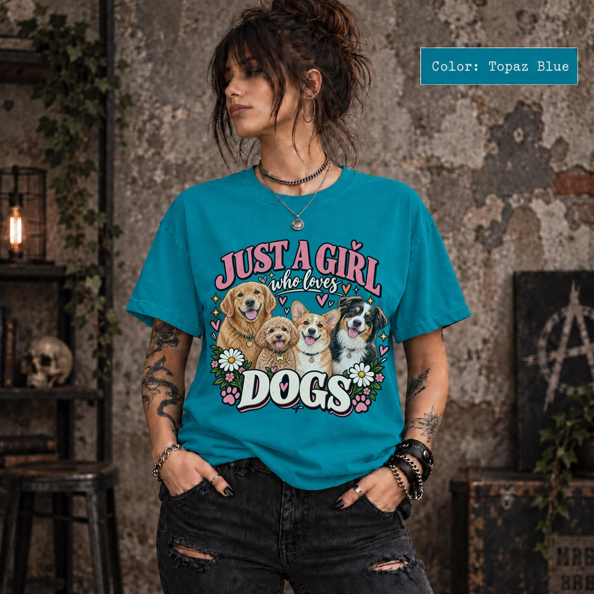 Woman modeling a Topaz blue graphic T-shirt featuring Just a Girl Who Loves Dogs design with four illustrated pups, pink and cream typography, hearts, daisies and paw prints.