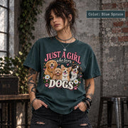 Woman modeling a blue spruce Comfort Colors T-shirt featuring a colorful dog mom design with four happy dogs, pink typography, white daisies and paw-print details.