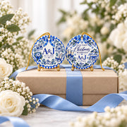 Two personalized blue porcelain-style wedding ornaments displayed on an elegant wrapped gift box with pale blue ribbon, white roses and delicate flowers, showcasing both design options.