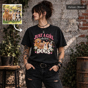 Woman wearing a black Comfort Colors 1717 T-shirt featuring Just a Girl Who Loves Dogs artwork with four smiling dogs, vintage pink lettering, flowers and paw prints, with a sample pet photo inset.