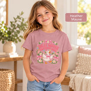 Smiling girl modeling a mauve pink birthday shirt with an adorable goose illustration, floral decorations, hearts and pink Silly Goose Birthday Girl typography.