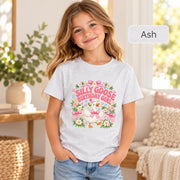 Smiling girl wearing a light ash gray Silly Goose birthday shirt decorated with a cheerful goose, pink ribbons, flowers and pastel-colored birthday details.