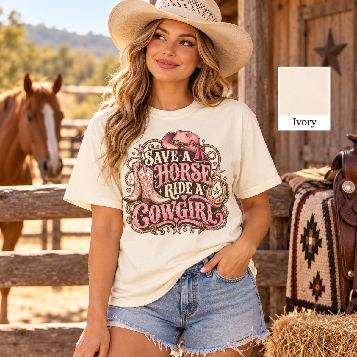 Blonde cowgirl wearing an ivory vintage Western graphic tee with pink save a horse ride a  cowgirl lettering, decorative stars and cowboy boot illustrations, standing beside a wooden ranch fence.