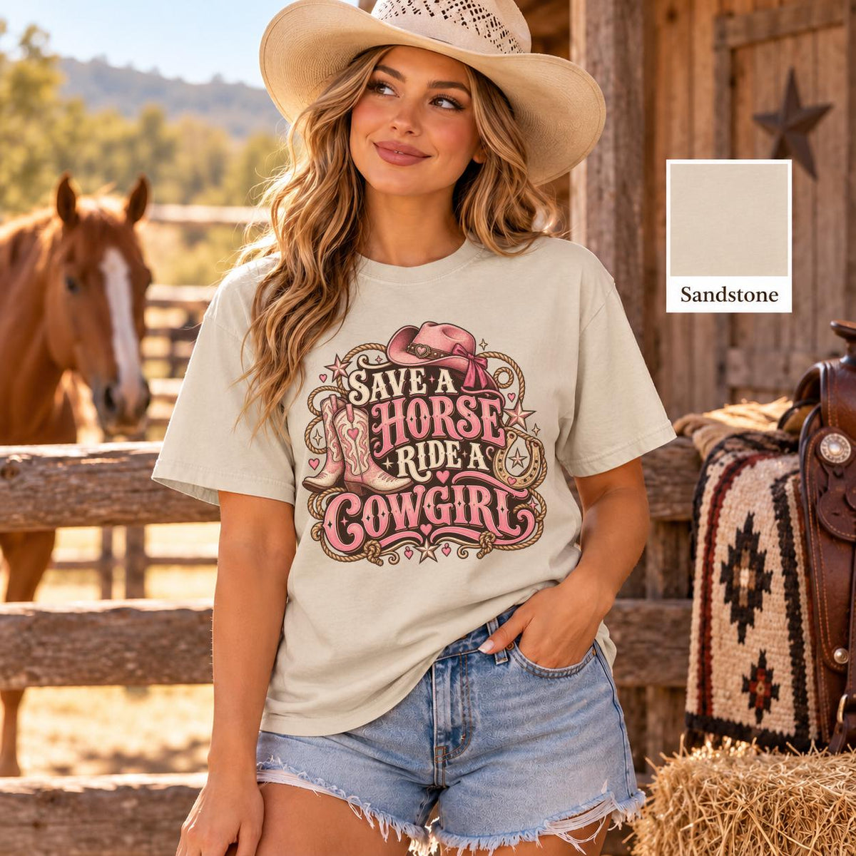 Woman modeling a sandstone Comfort Colors 1717 shirt with retro pink Save a horse ride a cowgirl graphic, Western hat and boots artwork, styled with denim shorts in warm outdoor lighting.