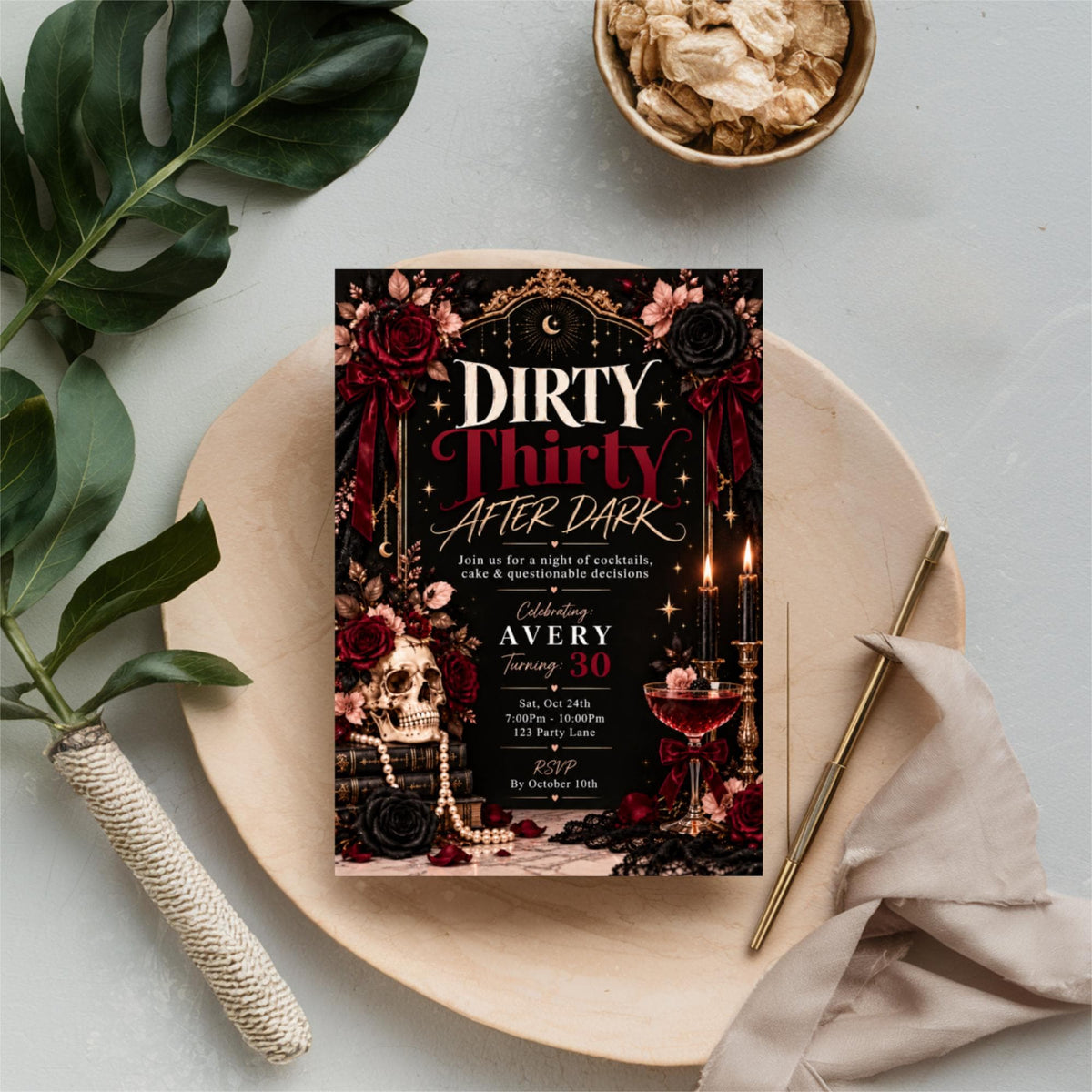 Editable Dirty Thirty birthday invitation resting on soft beige fabric beside botanical leaves and decorative accessories. Glamorous martini-themed 30th birthday party design with red and gold details.