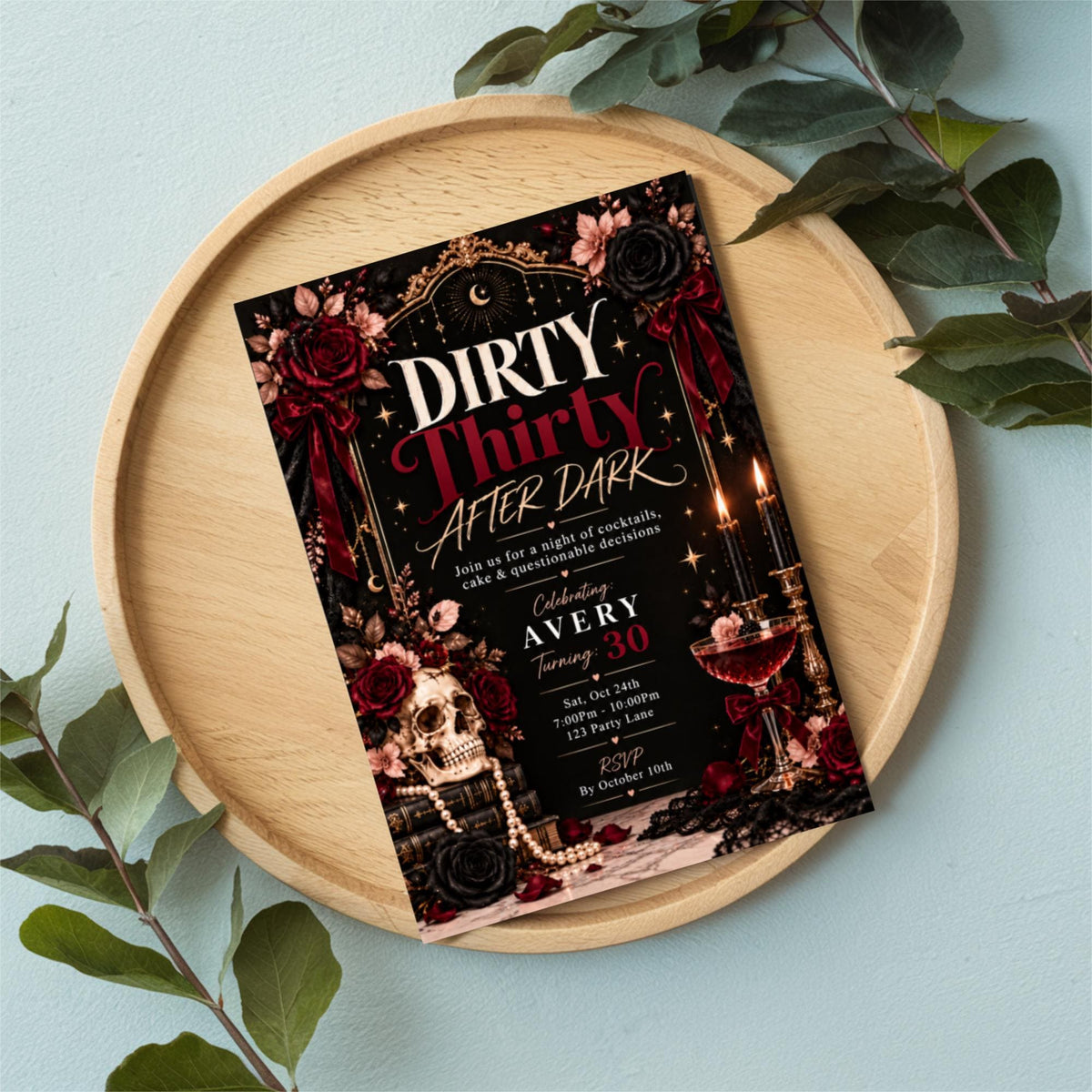 Dirty Thirty 30th birthday party invitation displayed inside a decorative tray with green leaves and elegant accessories. Chic black, burgundy, and gold design with martini-inspired birthday details.