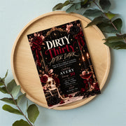 Dirty Thirty 30th birthday party invitation displayed inside a decorative tray with green leaves and elegant accessories. Chic black, burgundy, and gold design with martini-inspired birthday details.