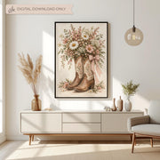 Vintage cowgirl poster featuring embroidered Western boots overflowing with pink daisies and ivory flowers. Displayed above a cream console table with dried grasses and simple decor.