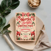 Vintage holiday party invitation resting on cream fabric beside greenery and coordinating Christmas decorations. The festive design features cheerful red lettering and playful Christmas-themed details.