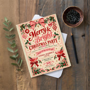 Vintage Christmas invitation displayed on a weathered wooden tabletop beside greenery and a dark decorative cup. The 5x7 holiday party template features traditional festive colours and nostalgic illustrations.