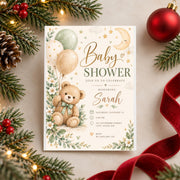 Watercolor baby shower invitation displayed against a Christmas-themed background with red ornaments and evergreen branches. The design features an adorable teddy bear, pastel balloons, delicate florals, and elegant baby shower lettering.