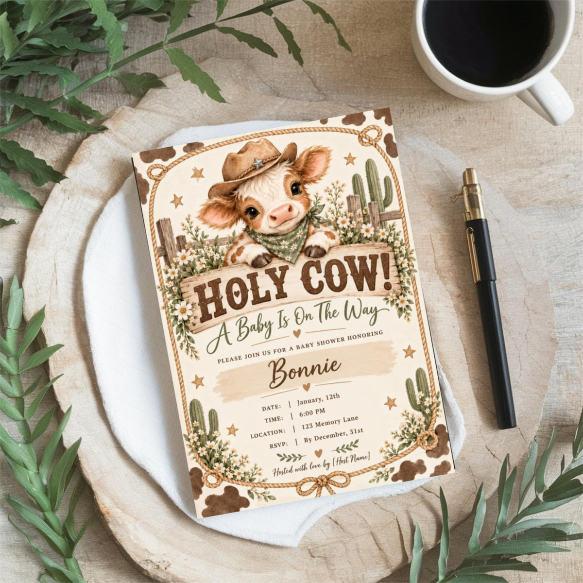 Western baby shower invitation displayed on a round white tray surrounded by botanical greenery and neutral decor. The rustic design features an adorable baby calf, cowboy hat, vintage lettering, and floral illustrations.