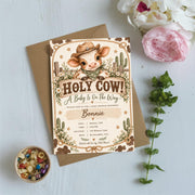 Cowboy-themed baby shower invitation displayed on a pale blue background surrounded by pink flowers and leafy greenery. The editable design features a baby calf, Western rope accents, daisies, and soft earthy colours.