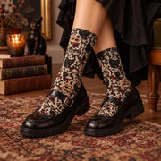 Gothic cat crew socks styled with black Mary Jane shoes and a dark skirt on a vintage rug. Features black, gray, and orange cats, red roses, bows, and celestial details on a cream background.