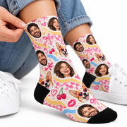 Personalized photo crew socks featuring custom faces of a man, woman, and corgi wearing heart-shaped sunglasses. Colorful pink checkerboard pattern with hearts, cherries, bows, and black toes and heels, styled with white sneakers.