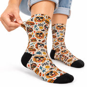 Close-up of playful dog socks featuring golden retrievers in sunglasses, colorful diner icons, checkerboard patterns, and smiley faces. Model gently stretches the fabric to show the printed design and texture.