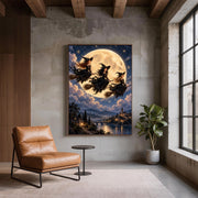 Gothic fantasy wall art displayed against a dark textured wall beside a tan leather chair. Three witches in flowing black dresses fly above a moonlit castle, river, and distant mountains.